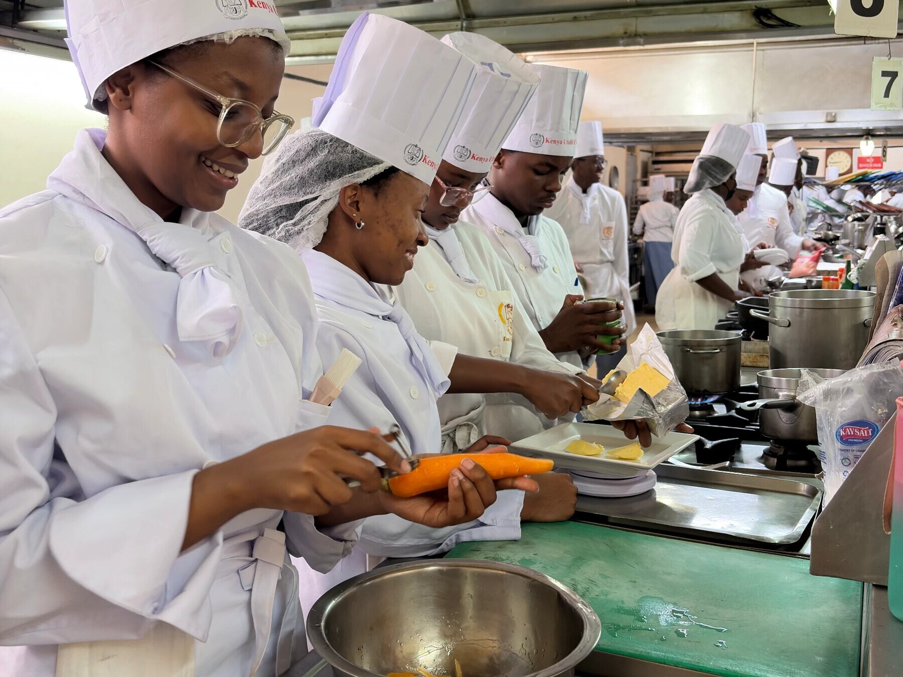 Students in chef whites preparing vegetables on a teaching kitchen line