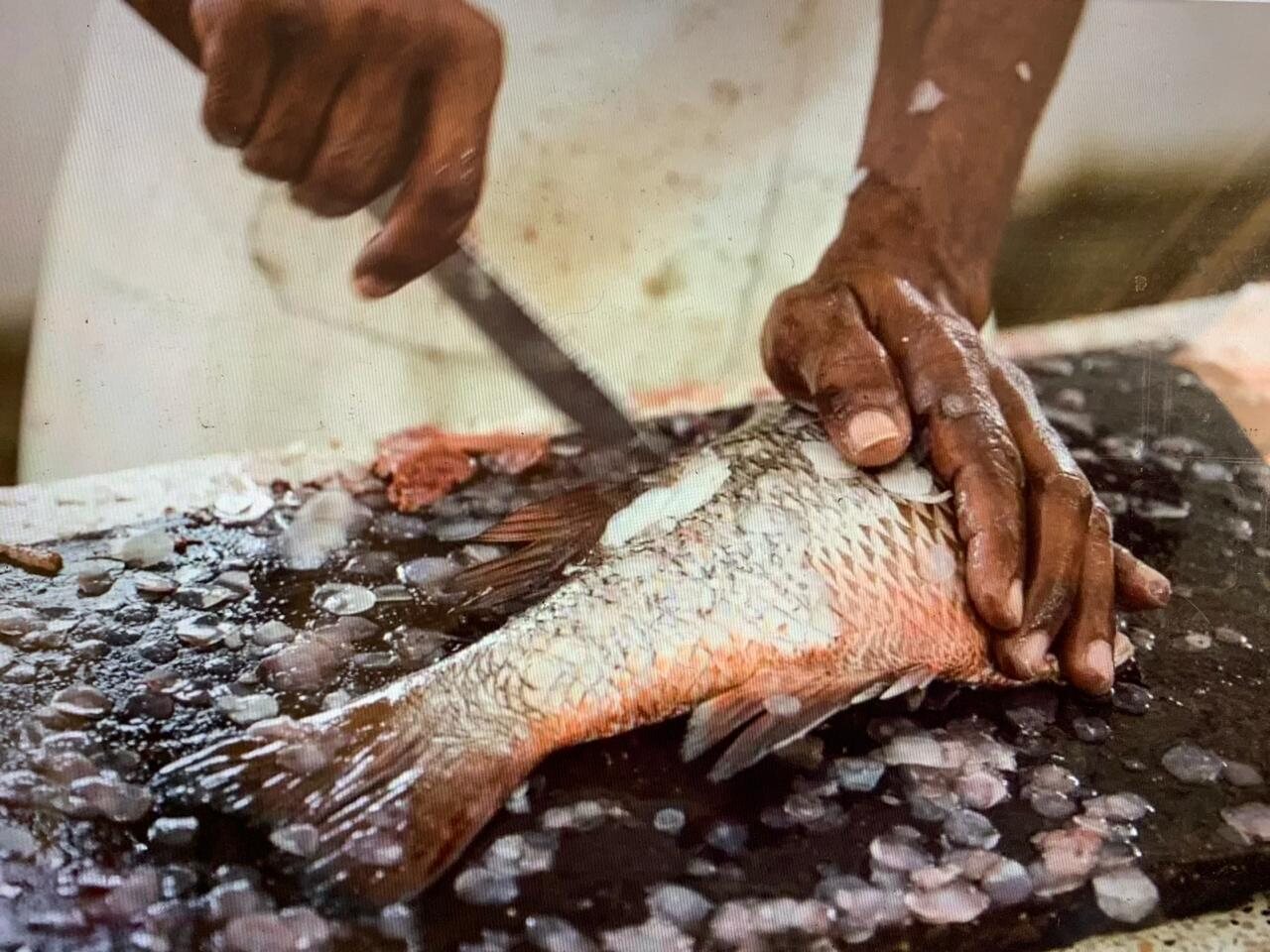 Hands filleting a large fresh fish on a dark cutting board